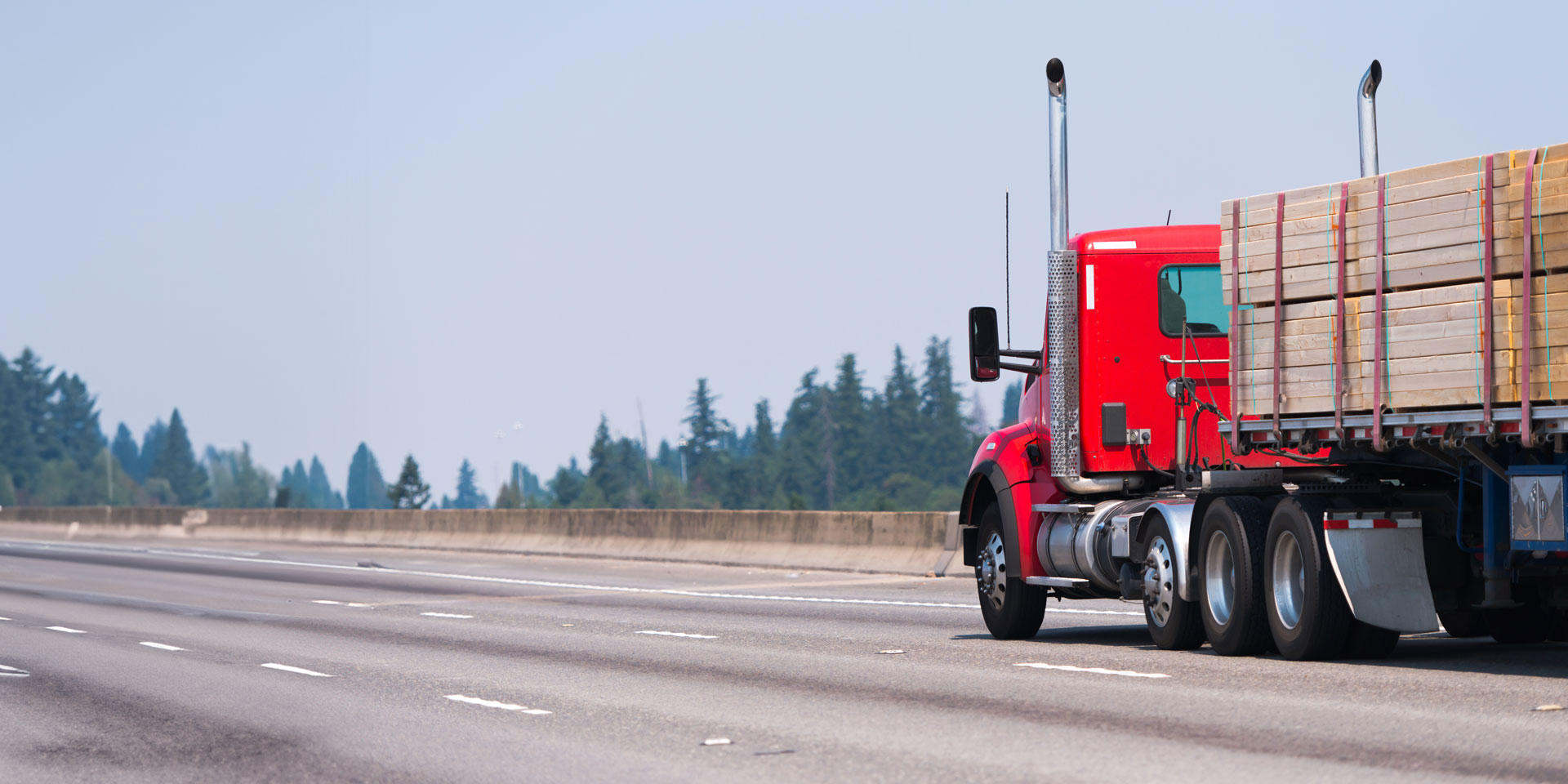 red semi truck hauling a flatbed load of treated wood